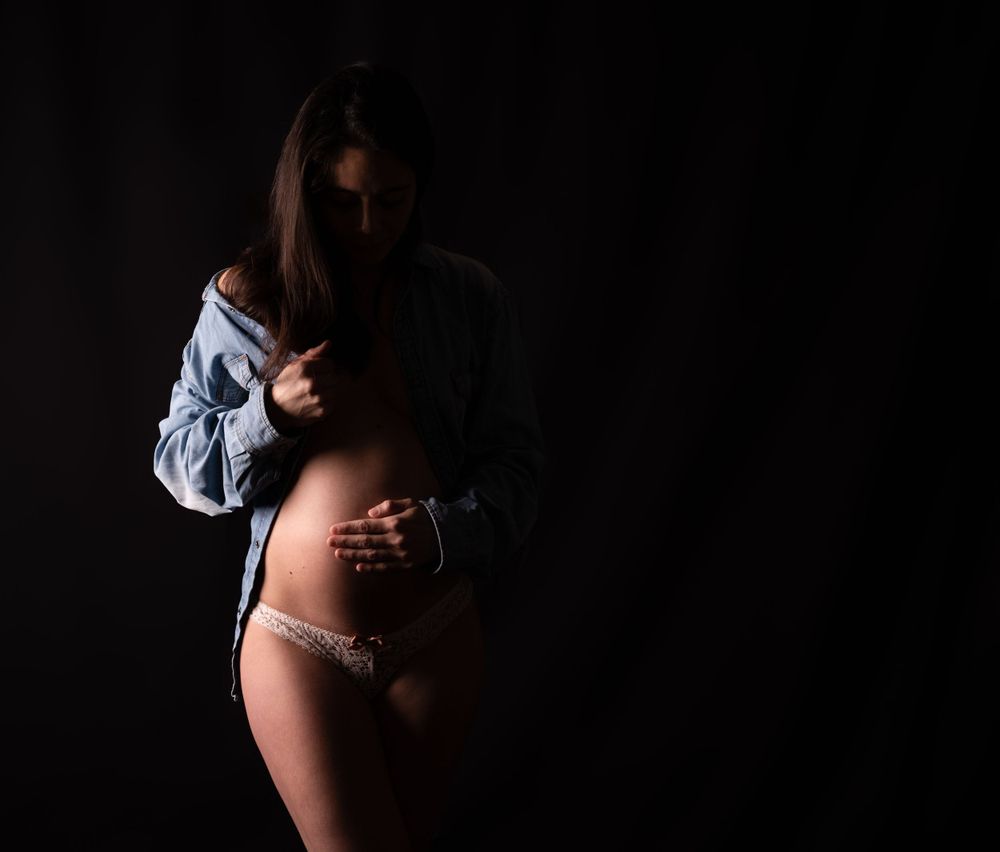 Soft sensual maternity portrait with denim shirt in low-key lighting.