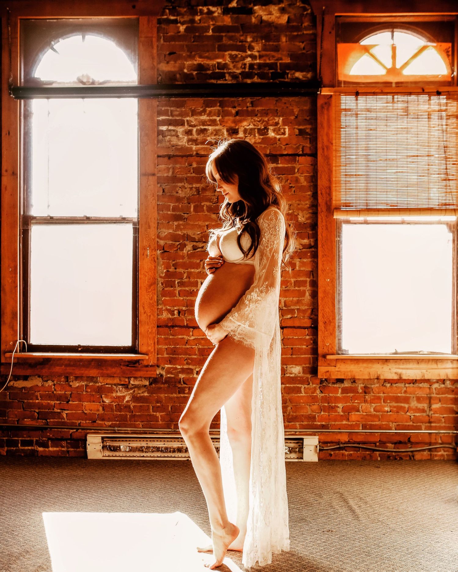 Maternity photoshoot in rustic brick loft with natural window lighting.