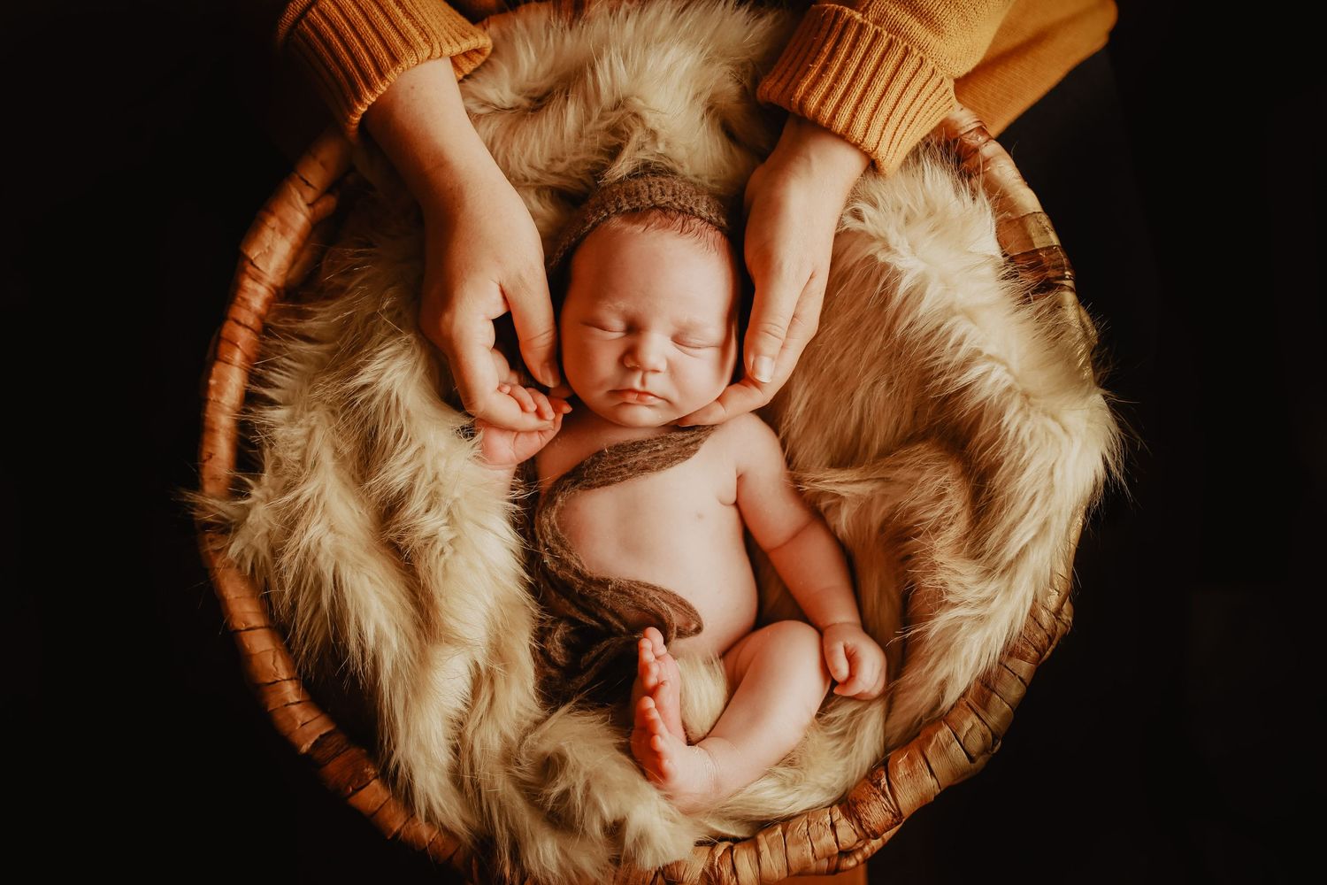 Newborn baby sleeping peacefully in soft beige fur blanket against dark background.