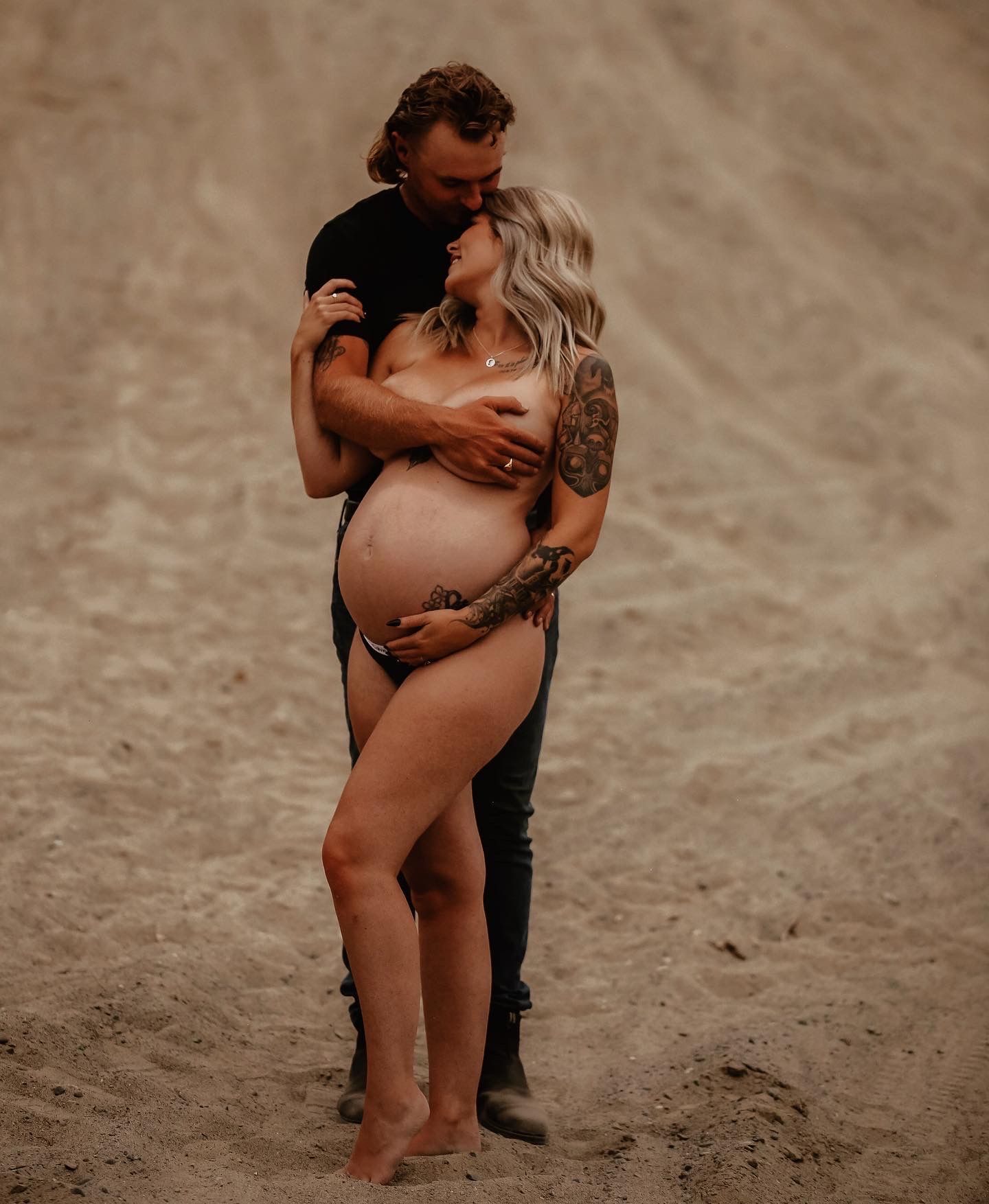 An intimate maternity portrait on a sandy beach at sunset.