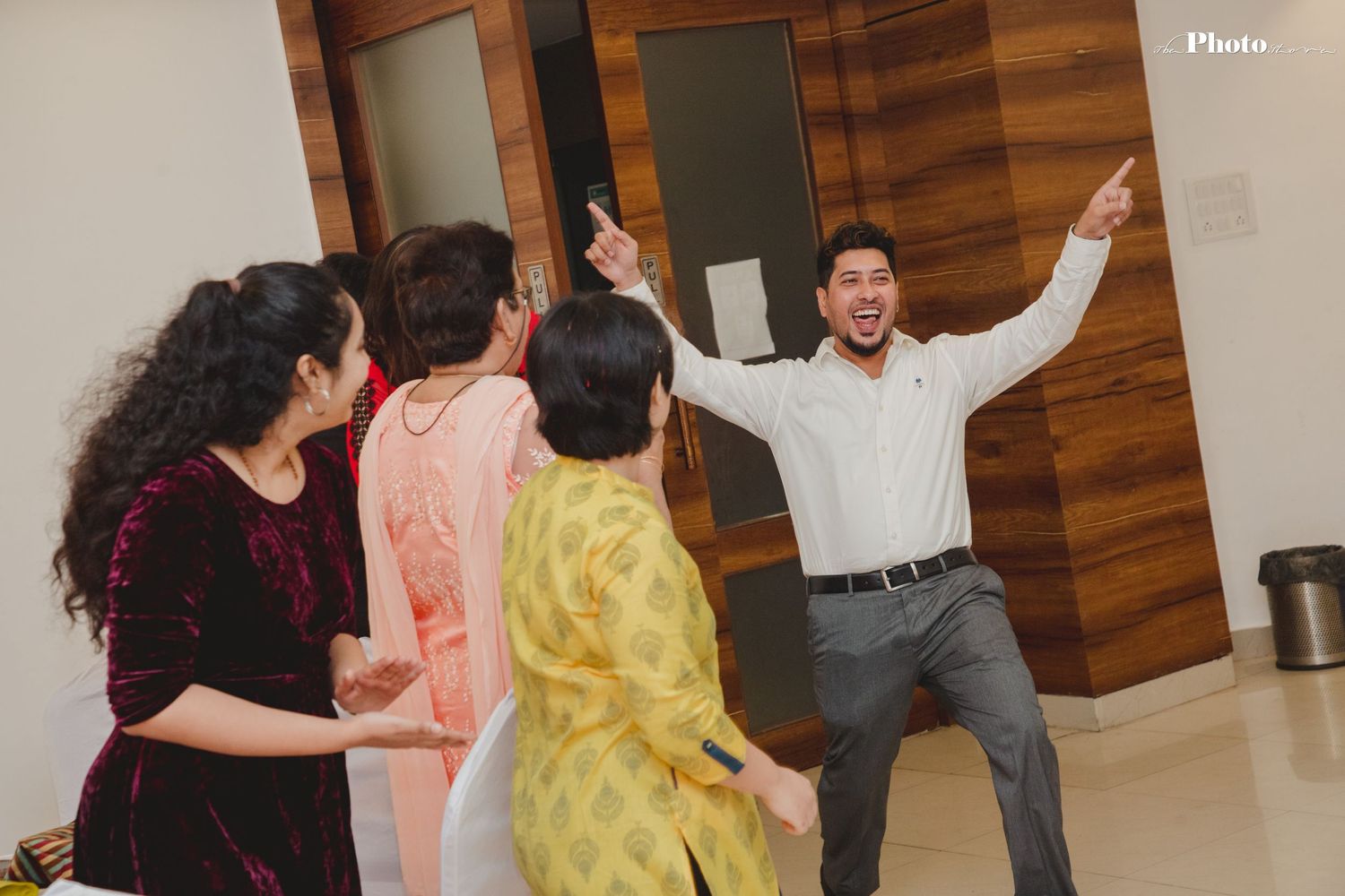People dancing and celebrating at an indoor party with wooden wall decor.