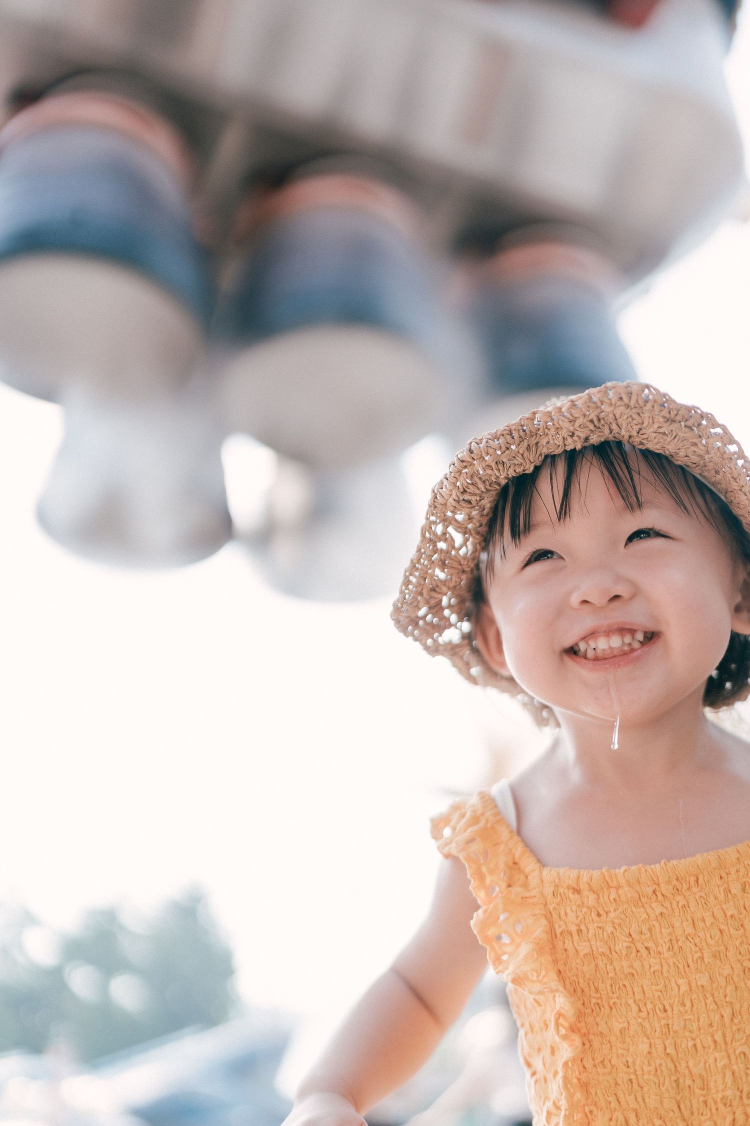 Child wearing a straw hat and yellow dress smiles brightly on a sunny day.