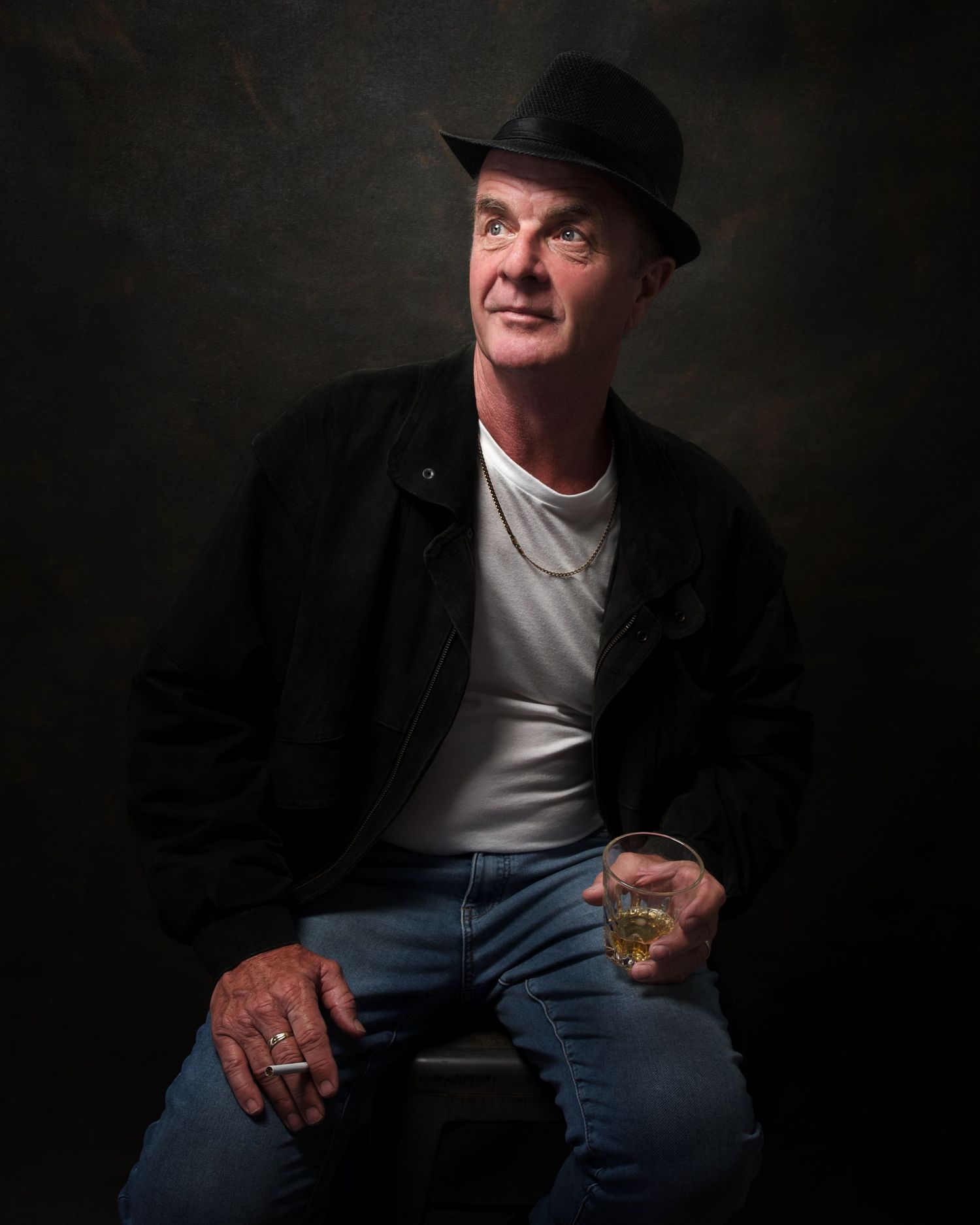 Classic painterly look portrait of a male holding a glass whiskey sitting on a stool