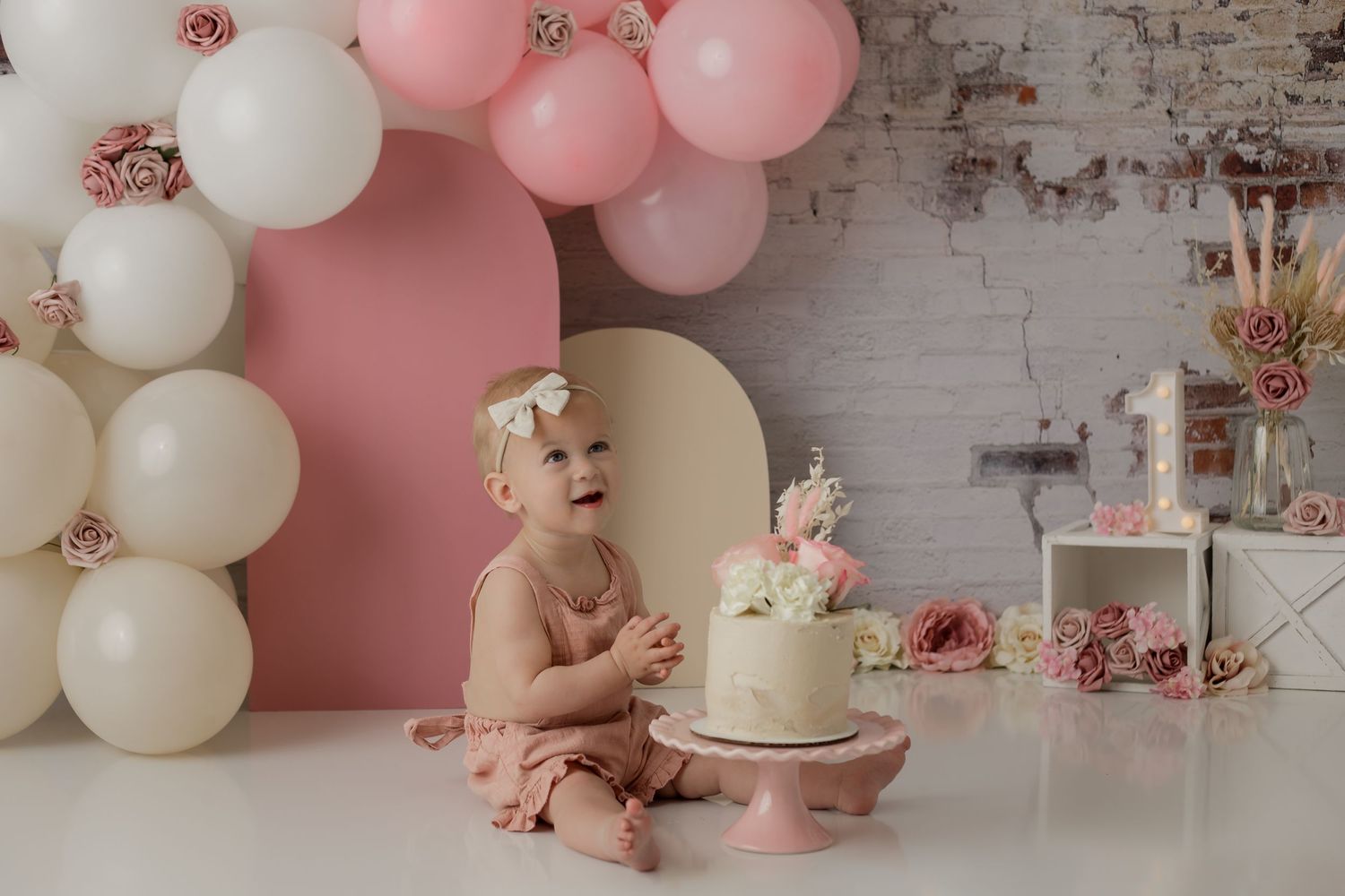 A custom floral theme setup with a baby girl wearing pink eating a cake for her studio cake smash photo session.