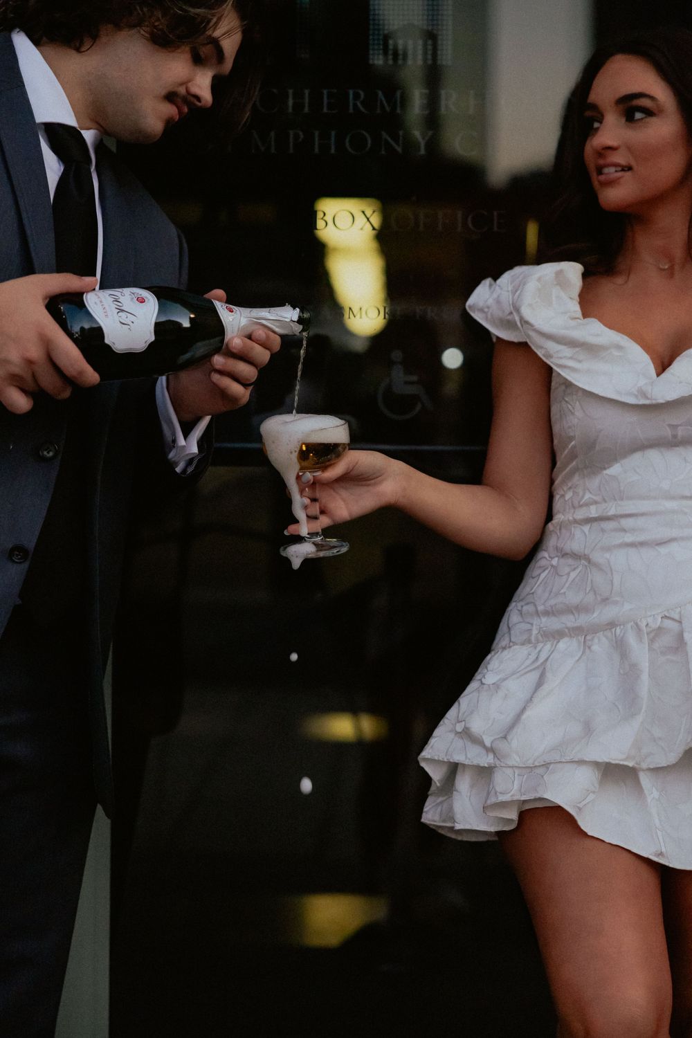 A couple in formal attire sharing champagne in an intimate dark setting.
