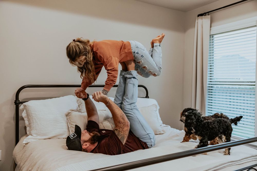 A playful indoor photoshoot on a bed with warm lighting and casual atmosphere.