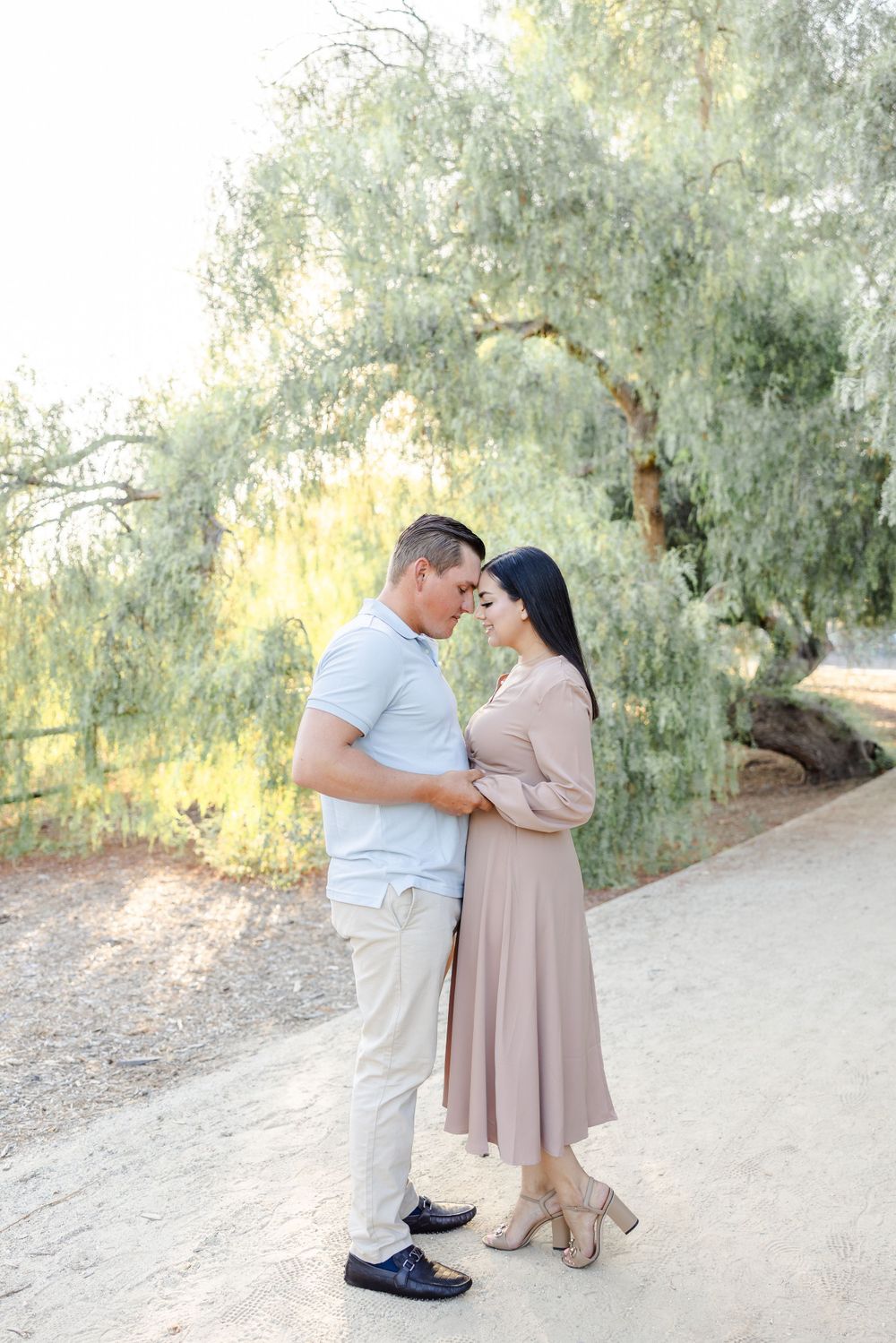 Couple dances together on a dirt path surrounded by willow trees and golden sunlight.