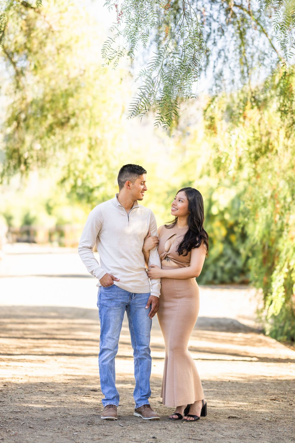 Couple takes romantic stroll under willow trees on sunny afternoon.