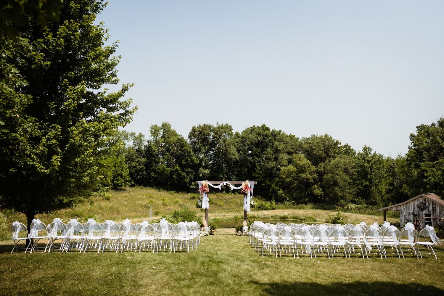 White chairs arranged in rows facing decorated wedding arch in outdoor garden setting.