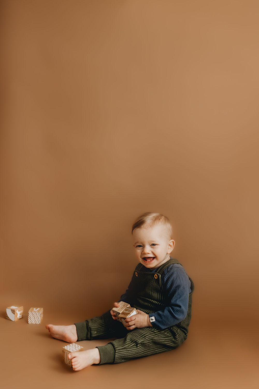 Smiling toddler in denim outfit sits on brown backdrop during studio photoshoot.