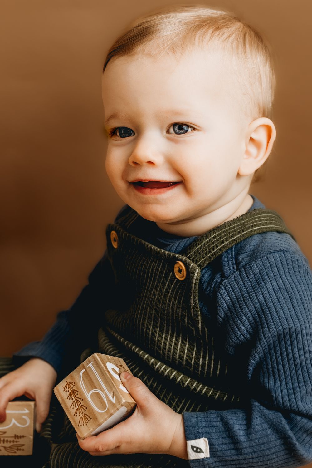 Happy baby in blue sweater and knit vest holding wooden blocks.