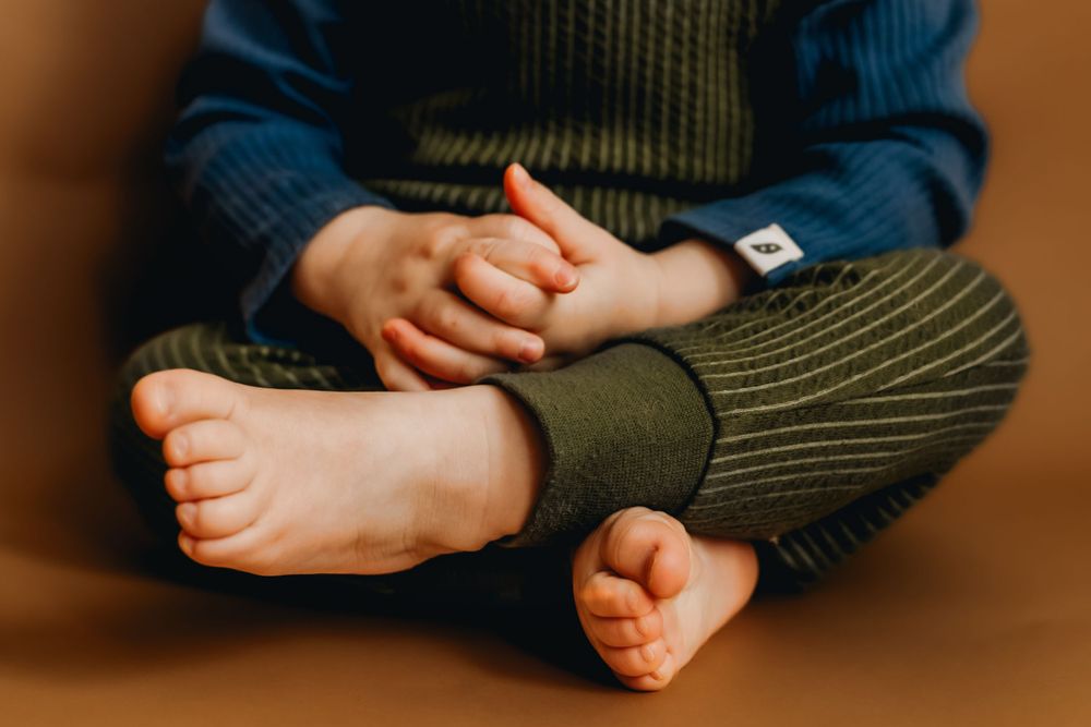 Close-up of small bare feet and hands in cozy knit clothing.