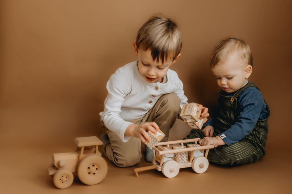 Two children playing with wooden toy train on brown background.