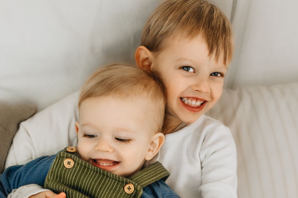 Two siblings sharing joyful moment together on white couch.