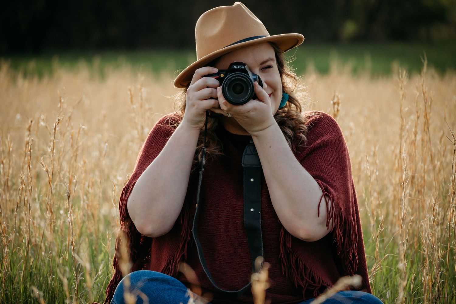 Photographer in burgundy poncho and brown hat taking pictures in a golden wheat field.