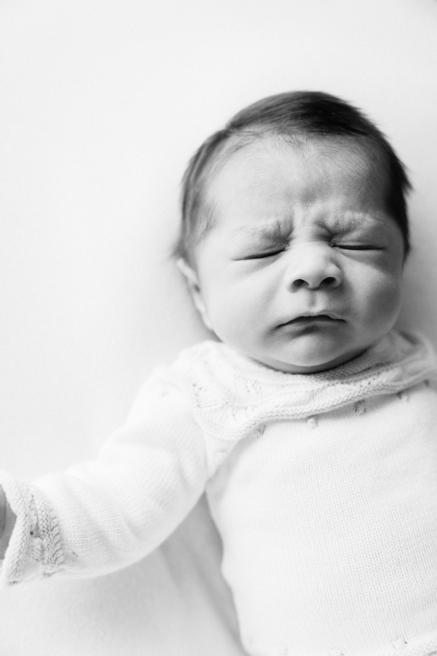 Black and white close-up portrait of sleeping newborn baby in white clothing.