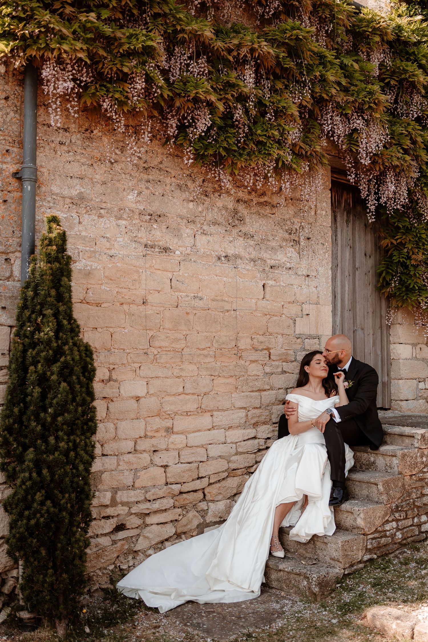 A couple cuddle on some stone steps in front of a wisteria covered building at Euridge Manor luxury wedding venue
