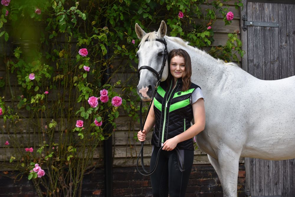 A white horse stands next to pink roses and a rustic barn door.