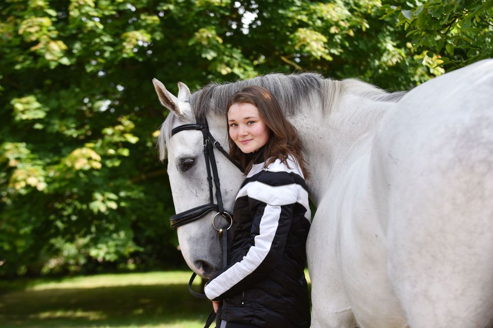 A white horse stands among green trees on a sunny day.