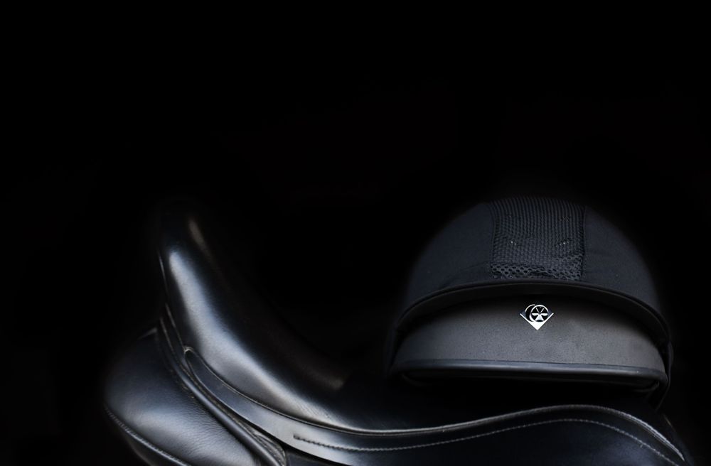 Close-up detail of black leather equestrian saddle against dark background.