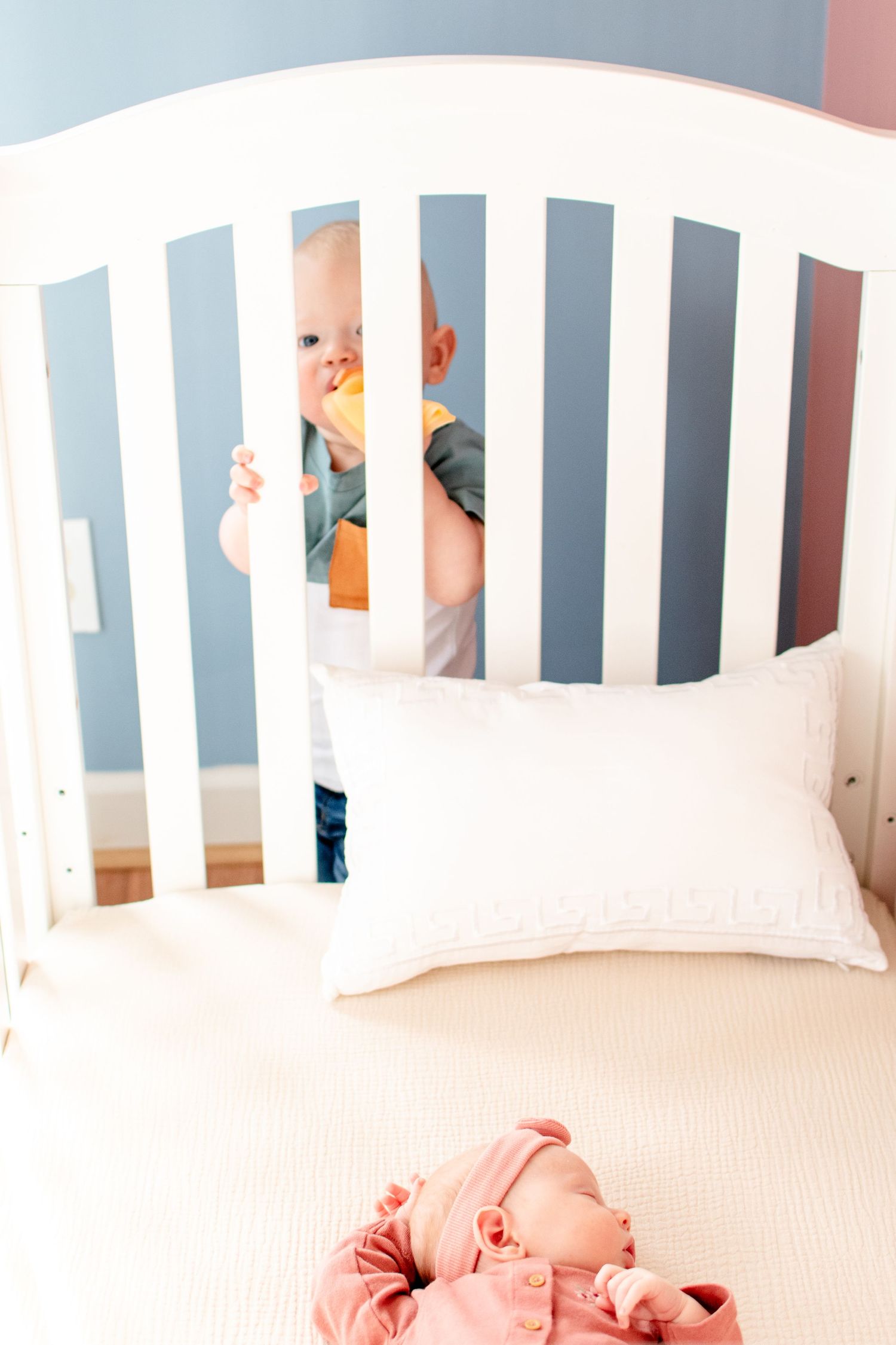 White crib with pillow and glimpse of baby through slats in nursery setting.