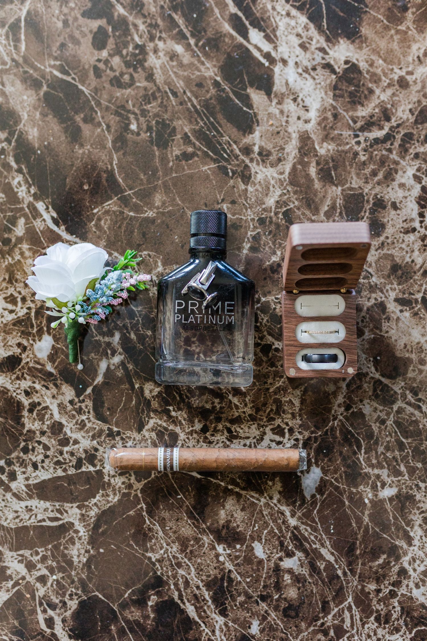 Wedding details featuring cologne, cigar, and accessories on dark marble surface.