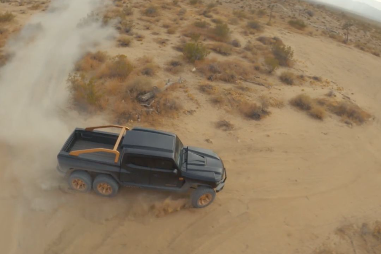 Black pickup truck driving on dusty desert road captured from aerial perspective.