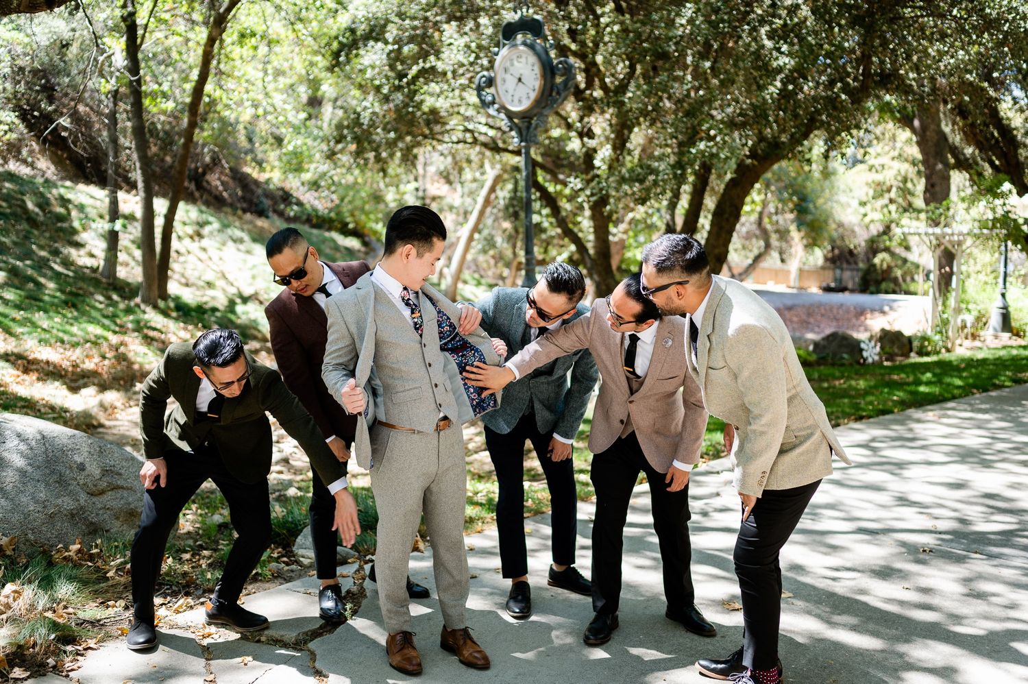 Groomsmen in formal attire posing outdoors on garden walkway.