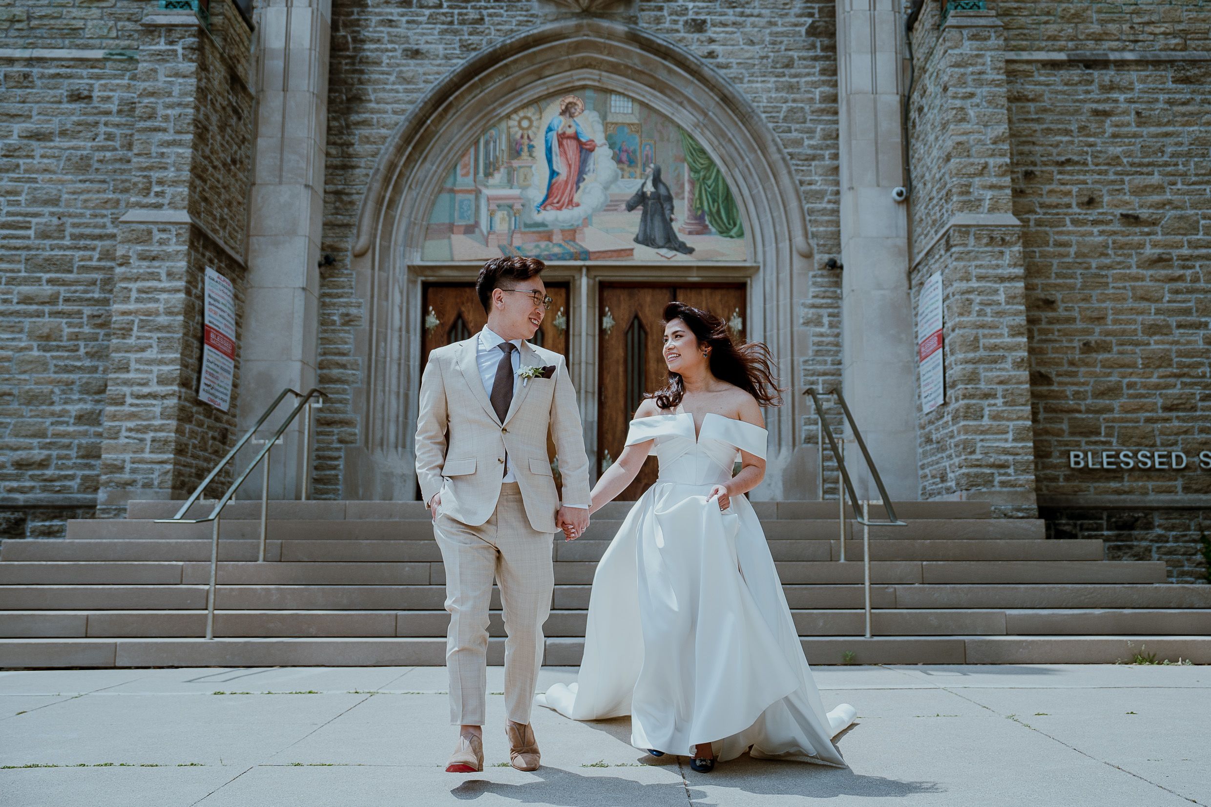 Couple poses on church steps in light wedding attire with architectural details.