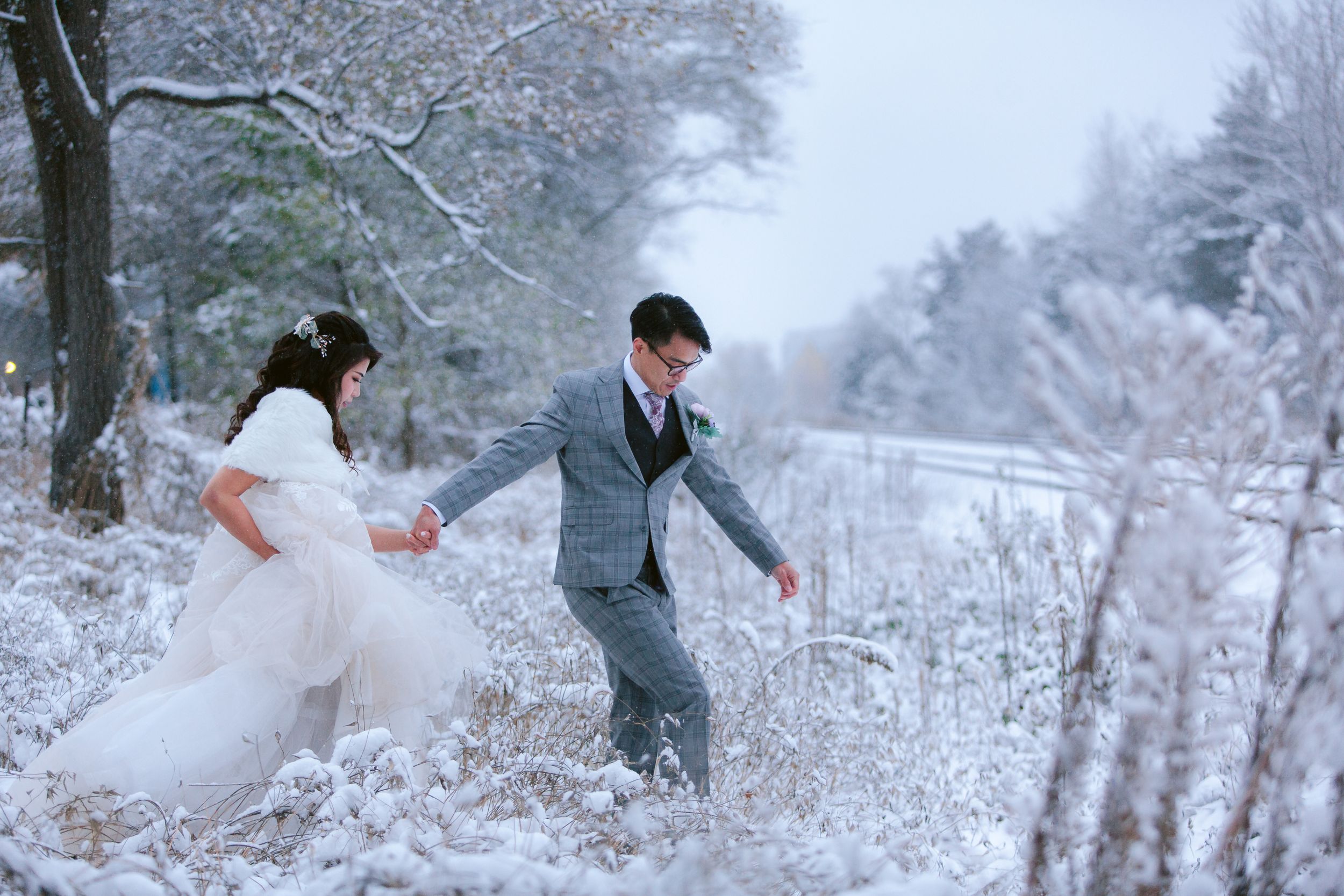 A newlywed couple playfully walks through a snow-covered winter landscape.