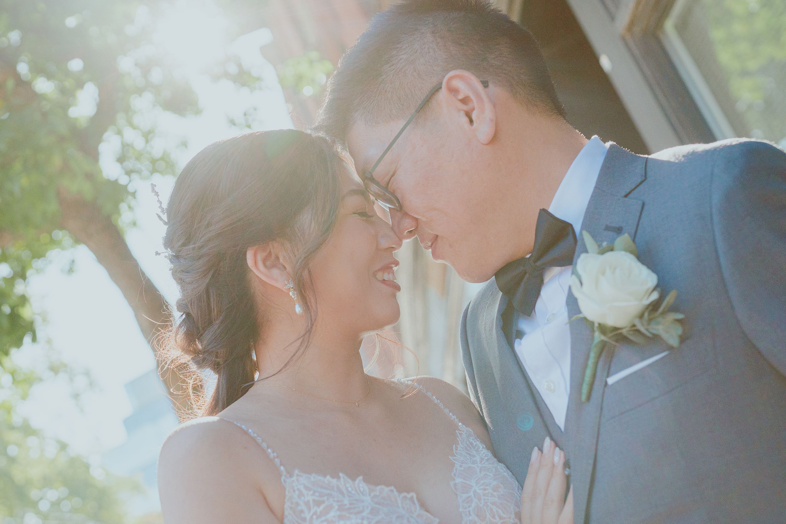 Tender romantic moment captured in soft sunlit outdoor wedding portrait.