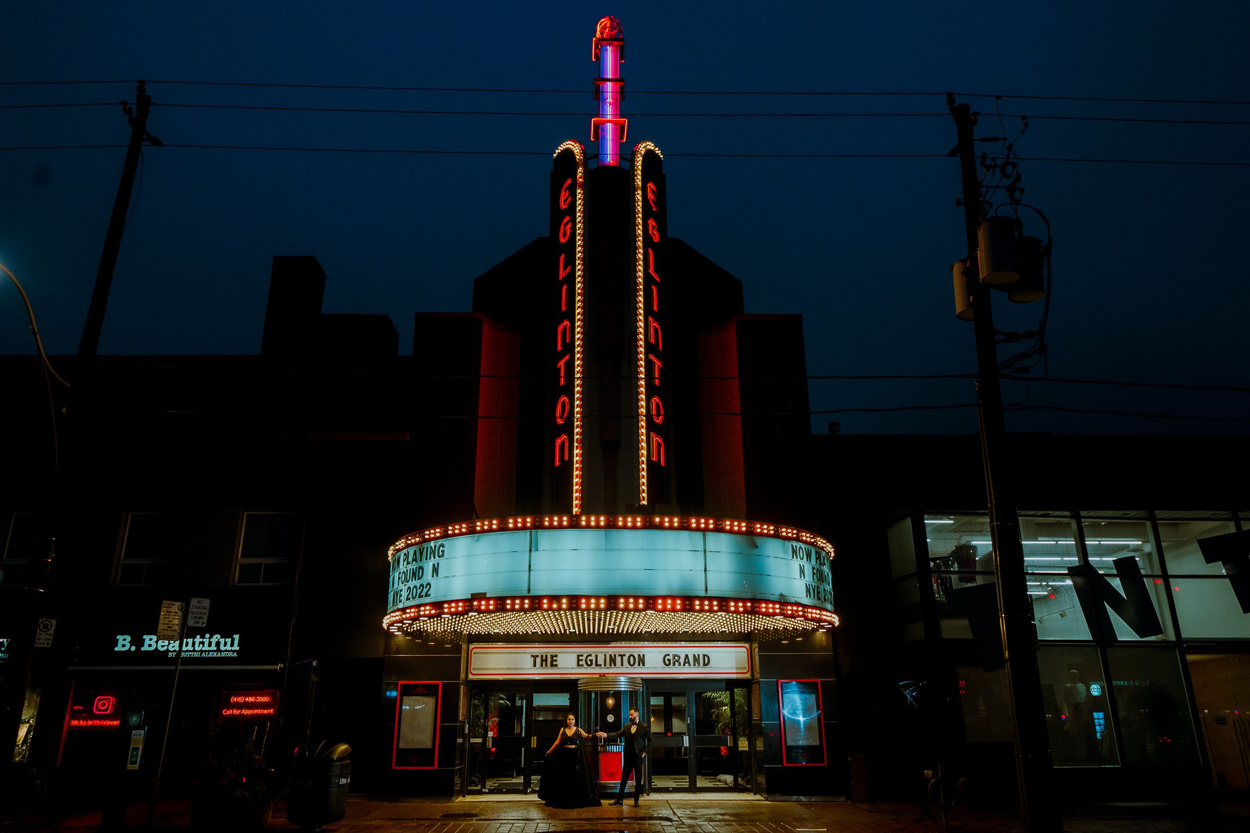 Vintage movie theater facade glows with neon lights against dark blue sky.
