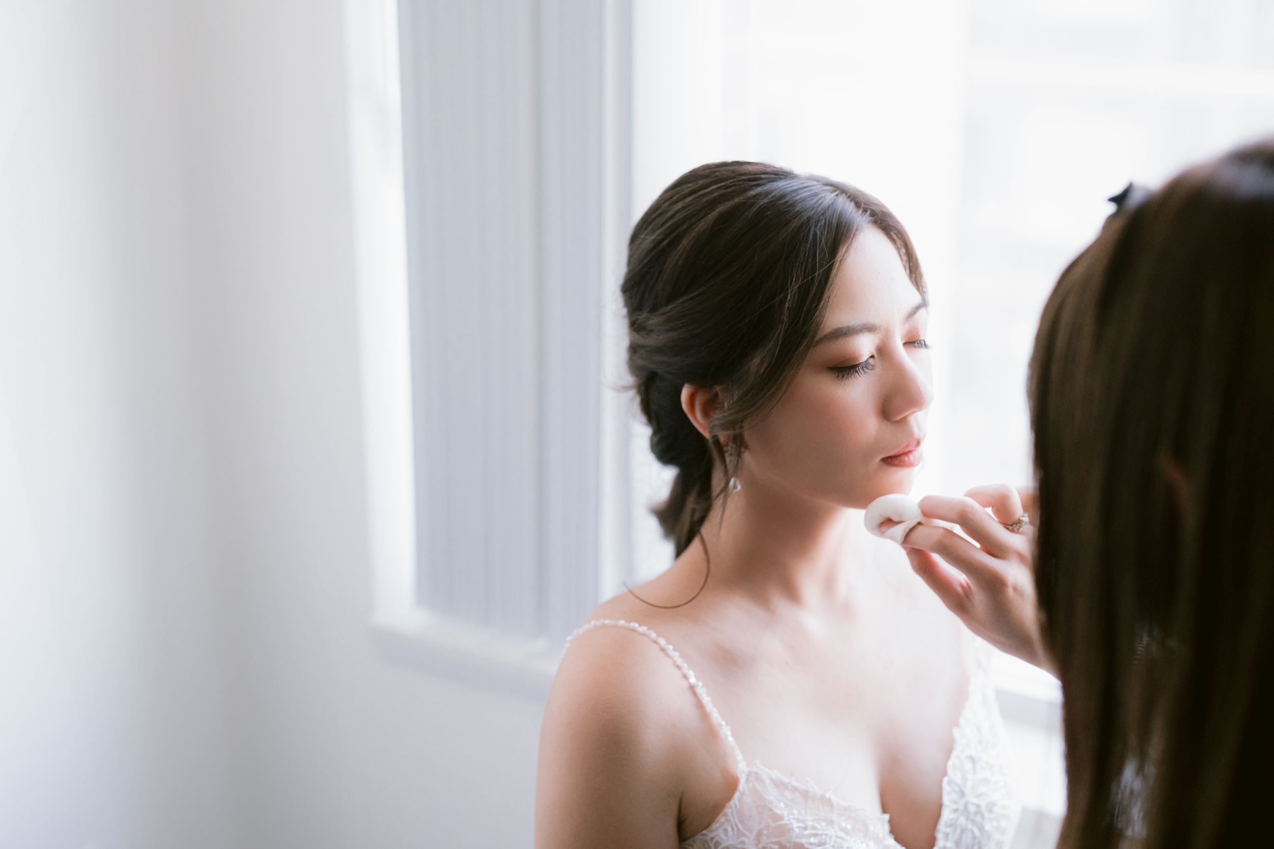 Soft natural window light illuminates intimate bridal preparation moment.