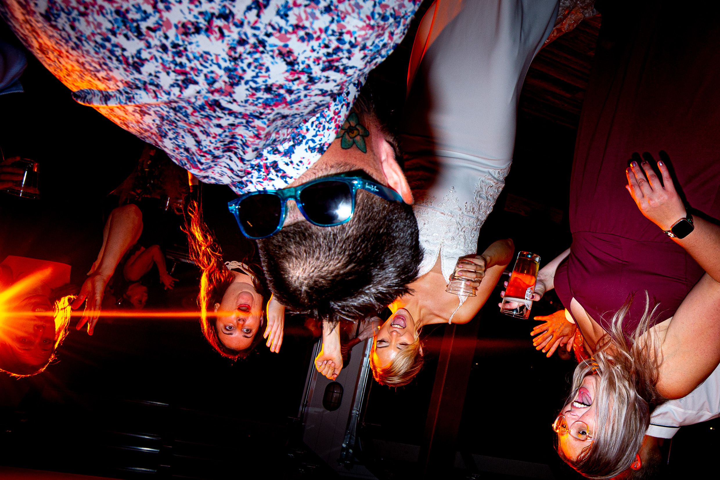 Wedding party dances energetically under colorful disco lights at reception.