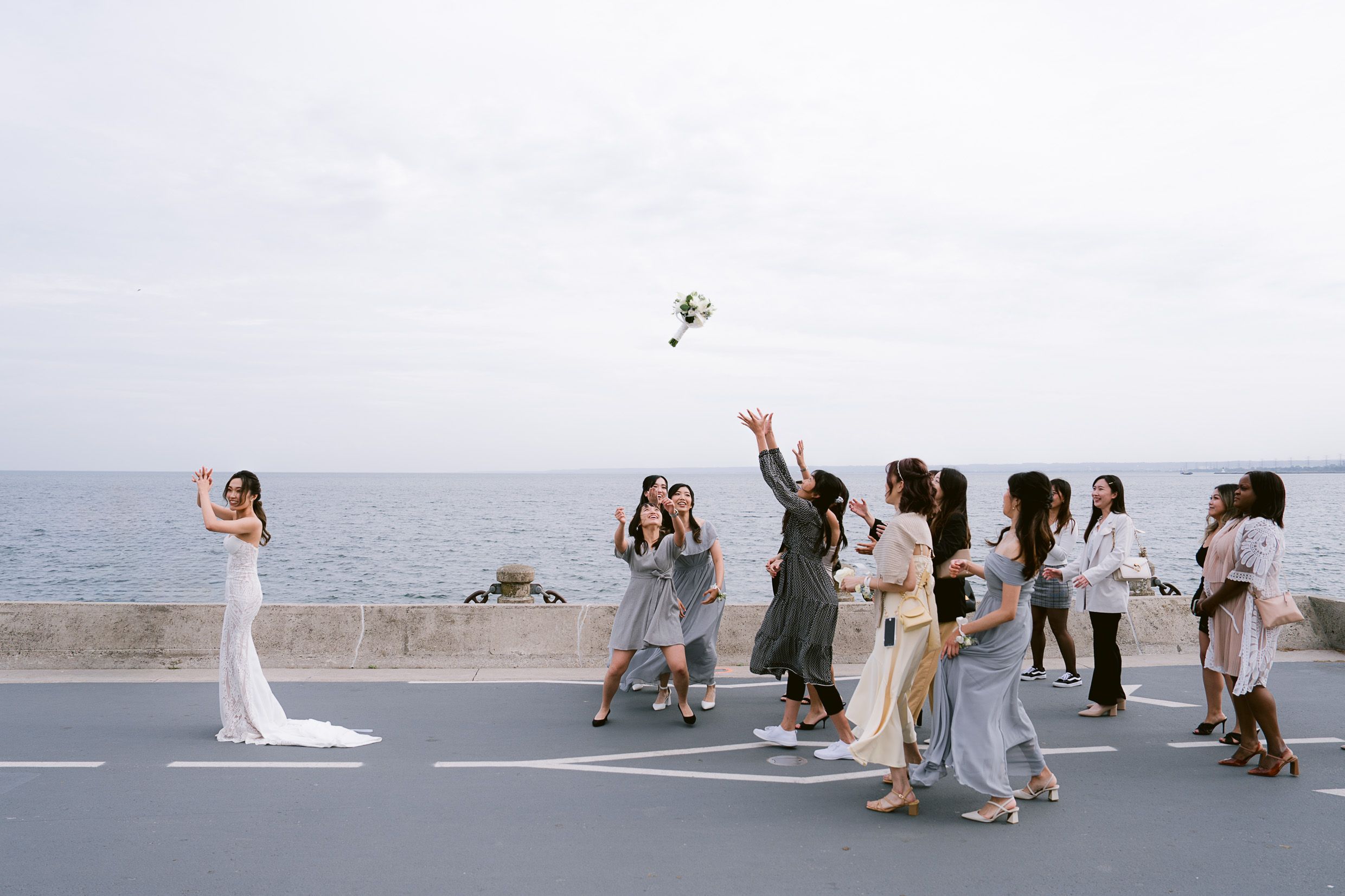 Wedding party on oceanfront throwing bouquet during sunset celebration.