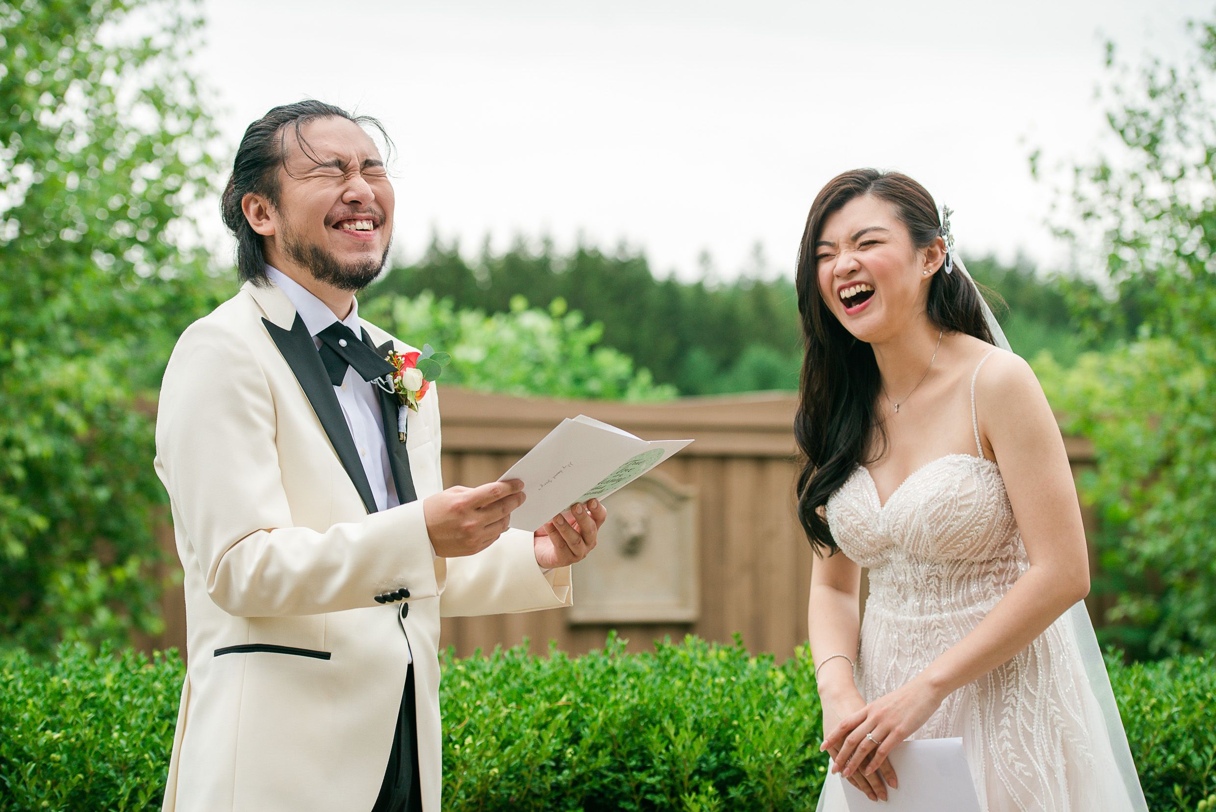 Joyful outdoor wedding moment with couple laughing in garden setting.