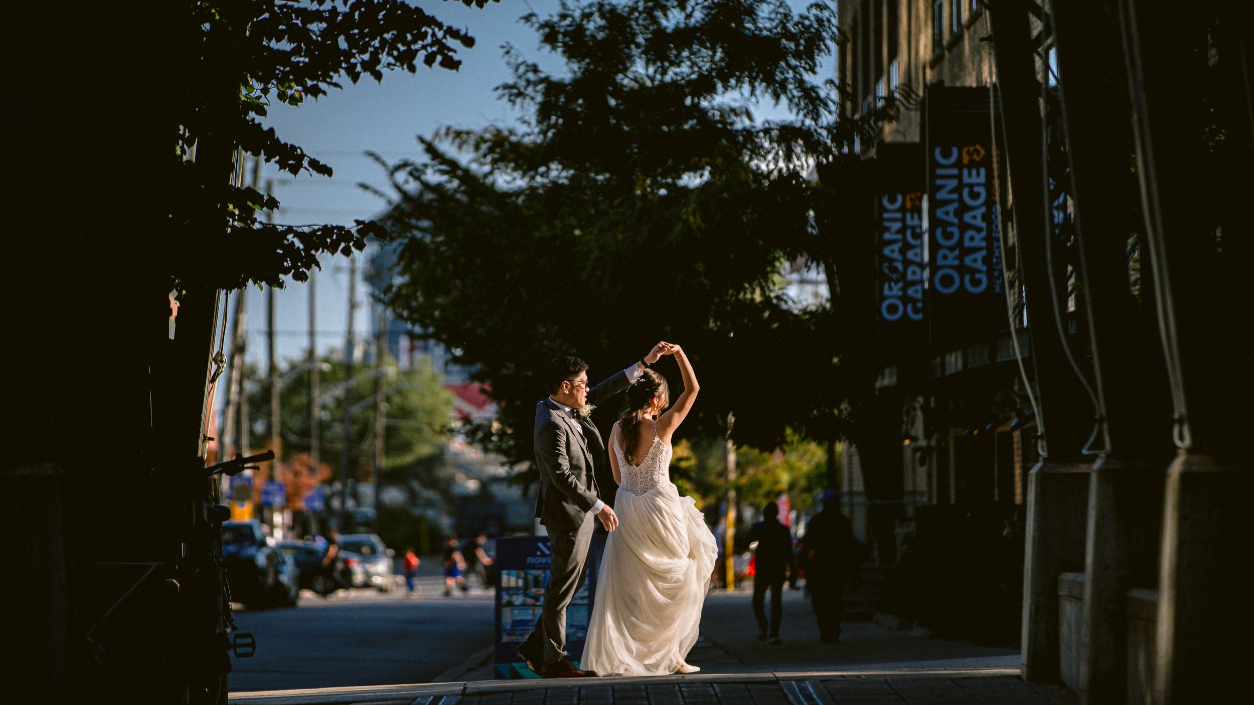 Wedding couple dances on urban street with city buildings in background.