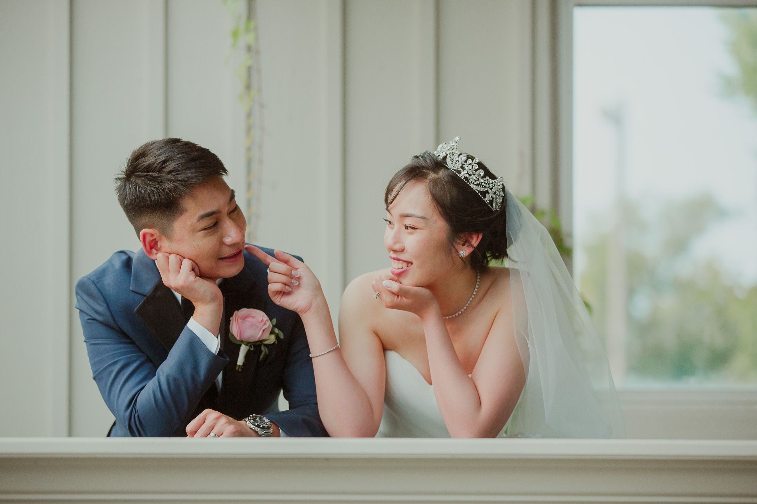 Playful wedding couple sharing an intimate moment near a bright window.
