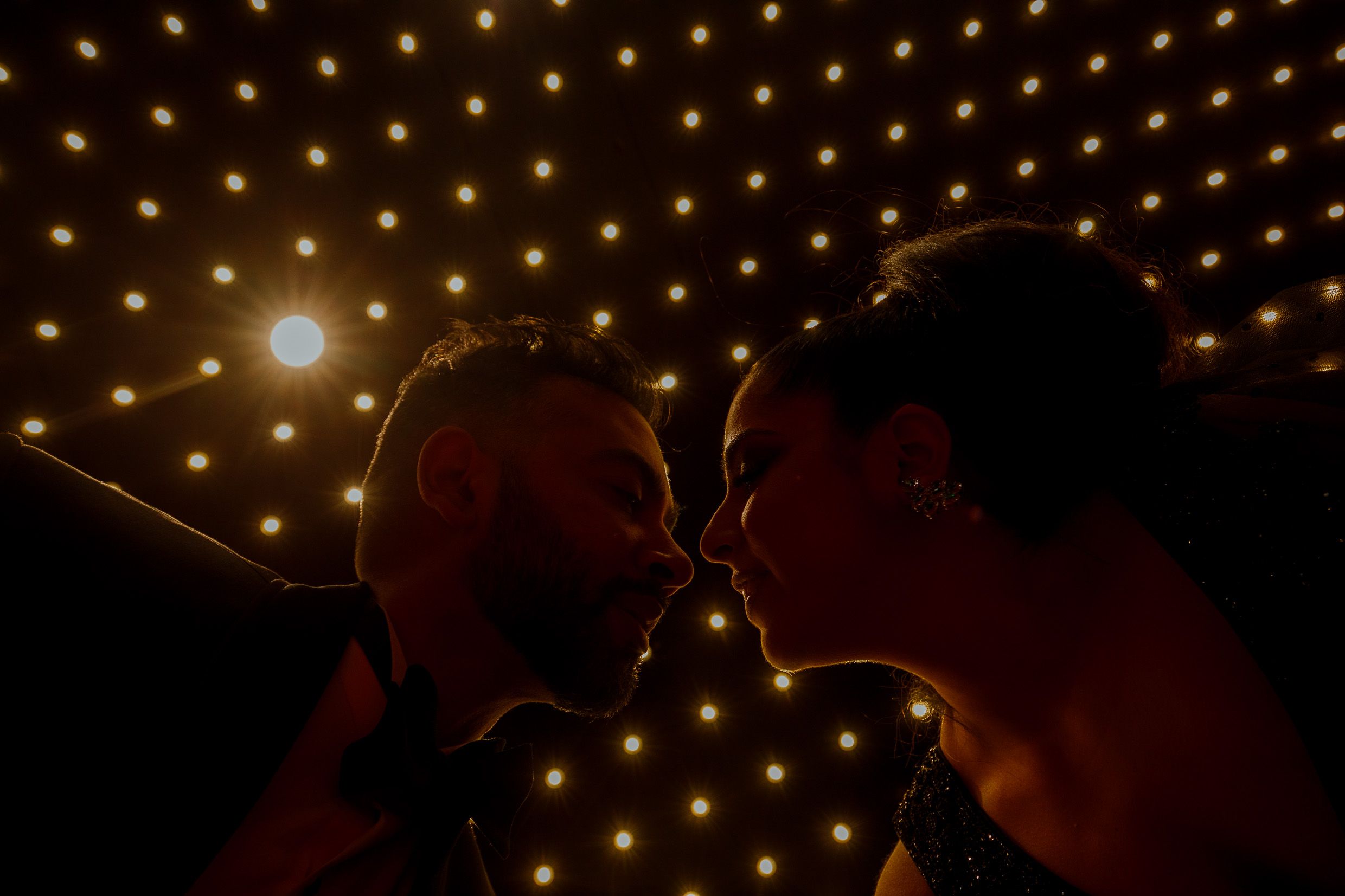 Silhouetted couple shares intimate moment beneath starry light installation.