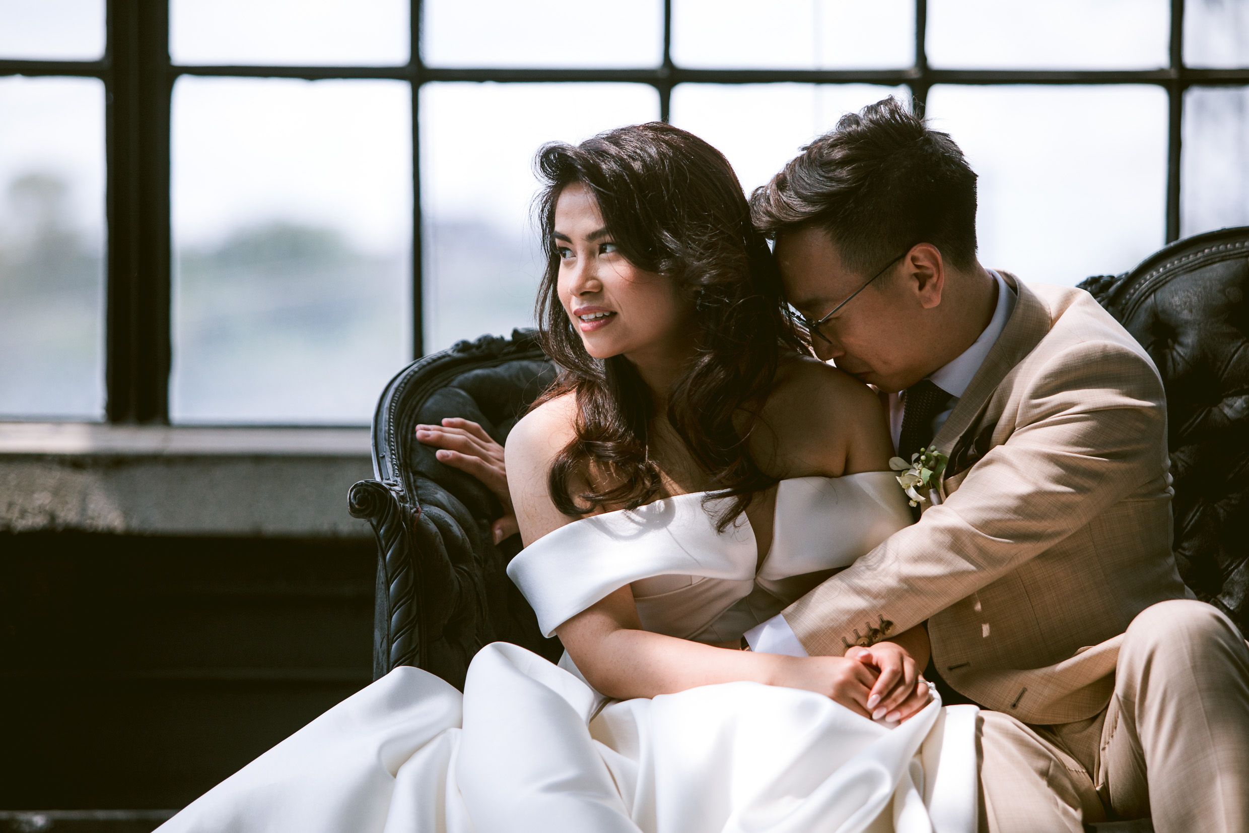 Couple relaxes together on vintage leather couch by window in intimate moment.