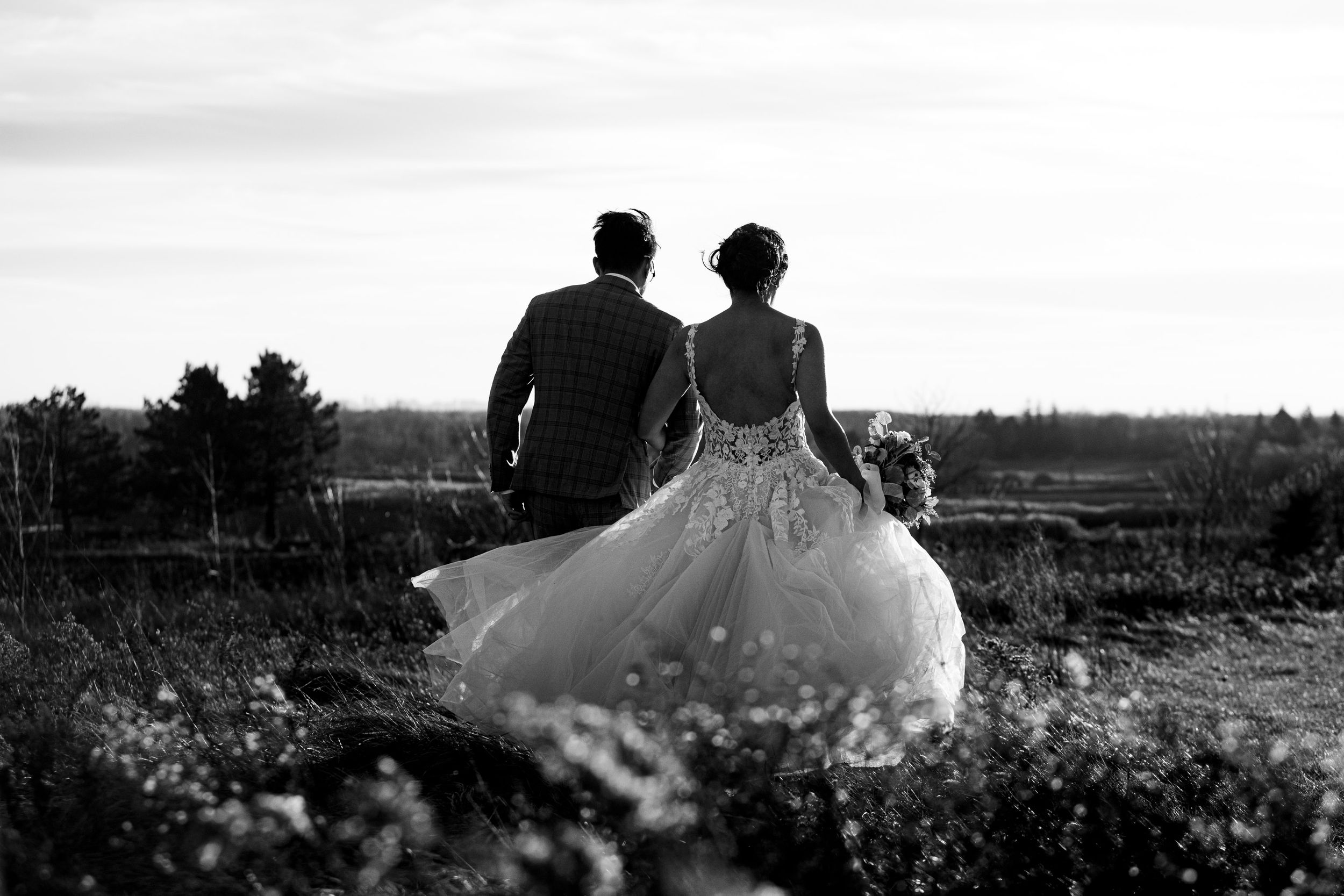 Black and white photo of newlyweds sitting together on a hill overlooking a landscape.