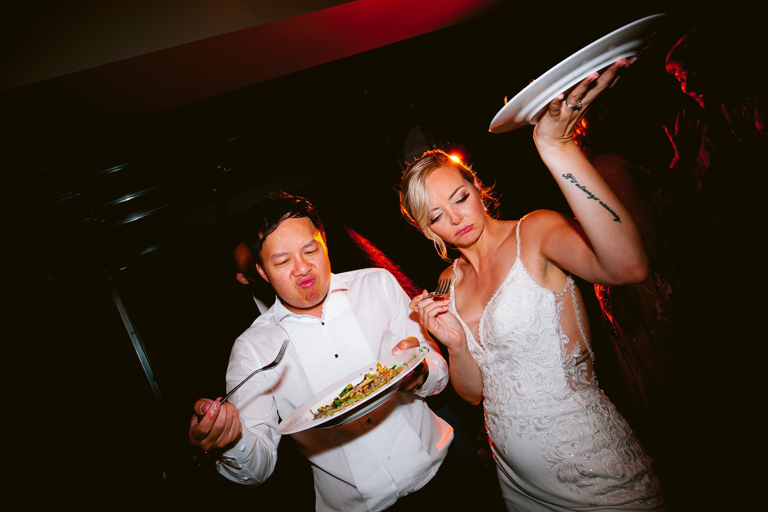 Couple joyfully sharing food during wedding reception celebration.