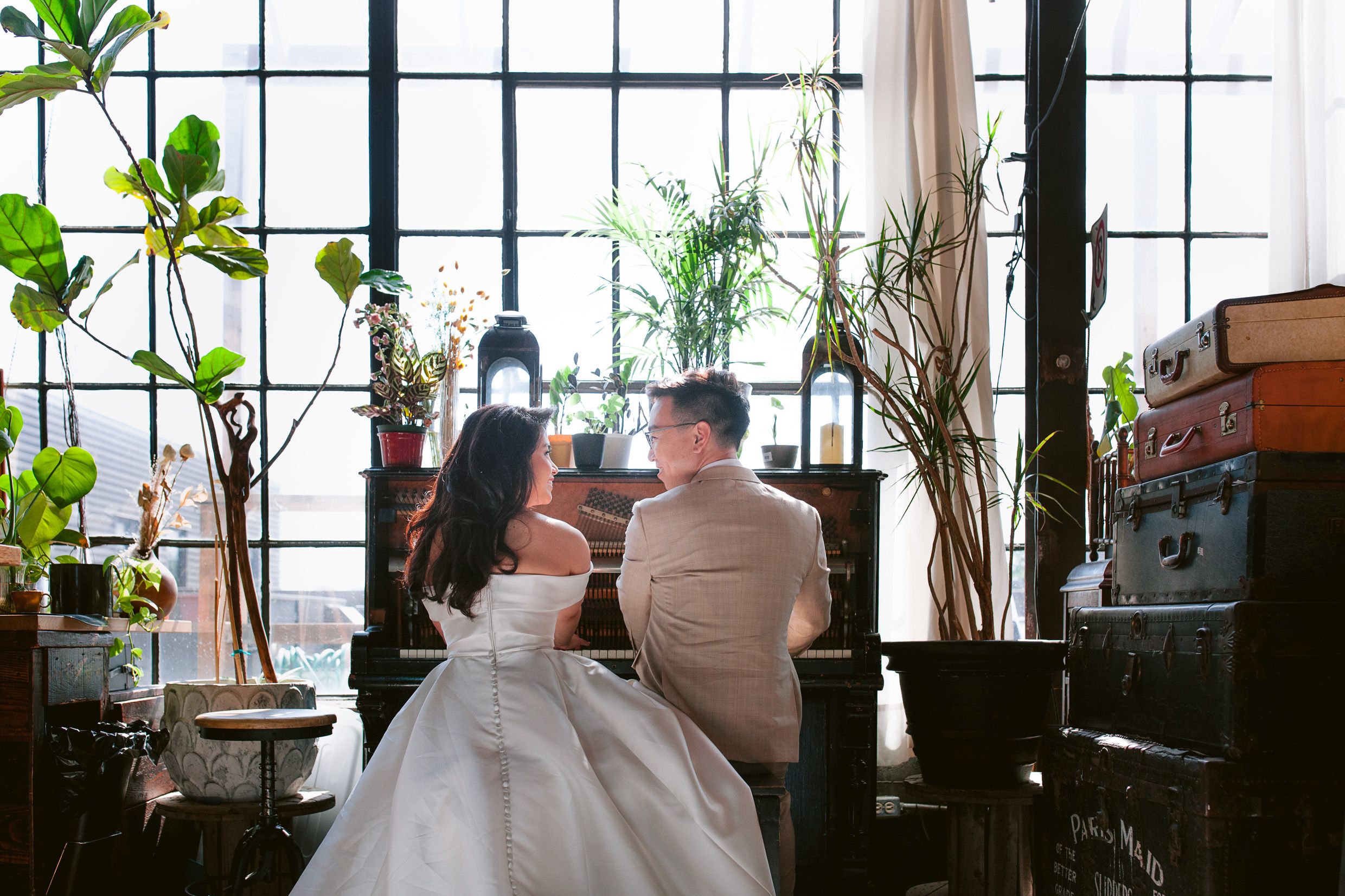 A couple sits intimately by large windows surrounded by indoor plants in an urban loft space.