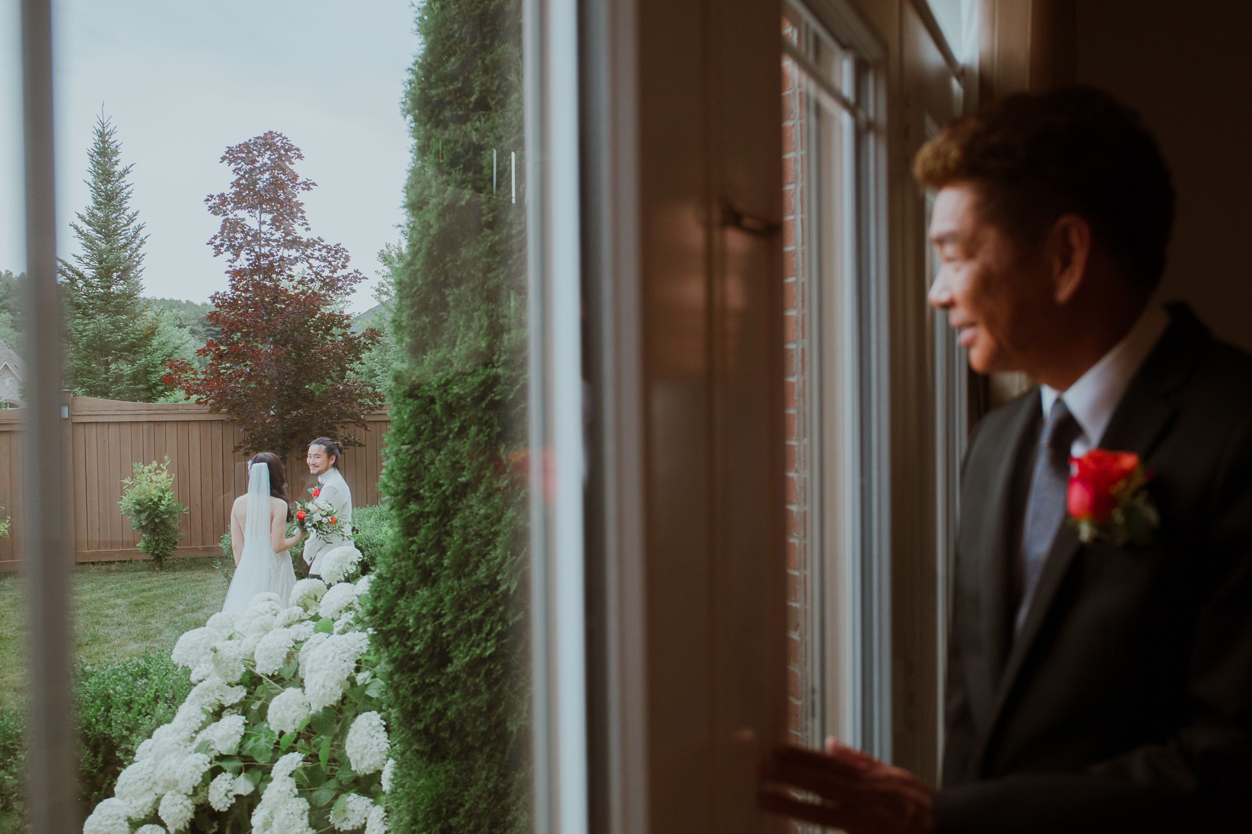 Quiet moment through window showing wedding scene with greenery outside.