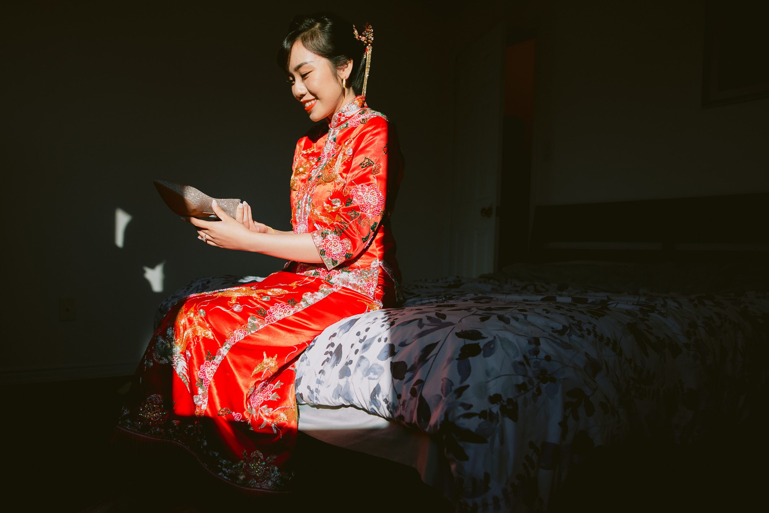 Woman in traditional red Chinese dress sitting on bed looking at mobile device.