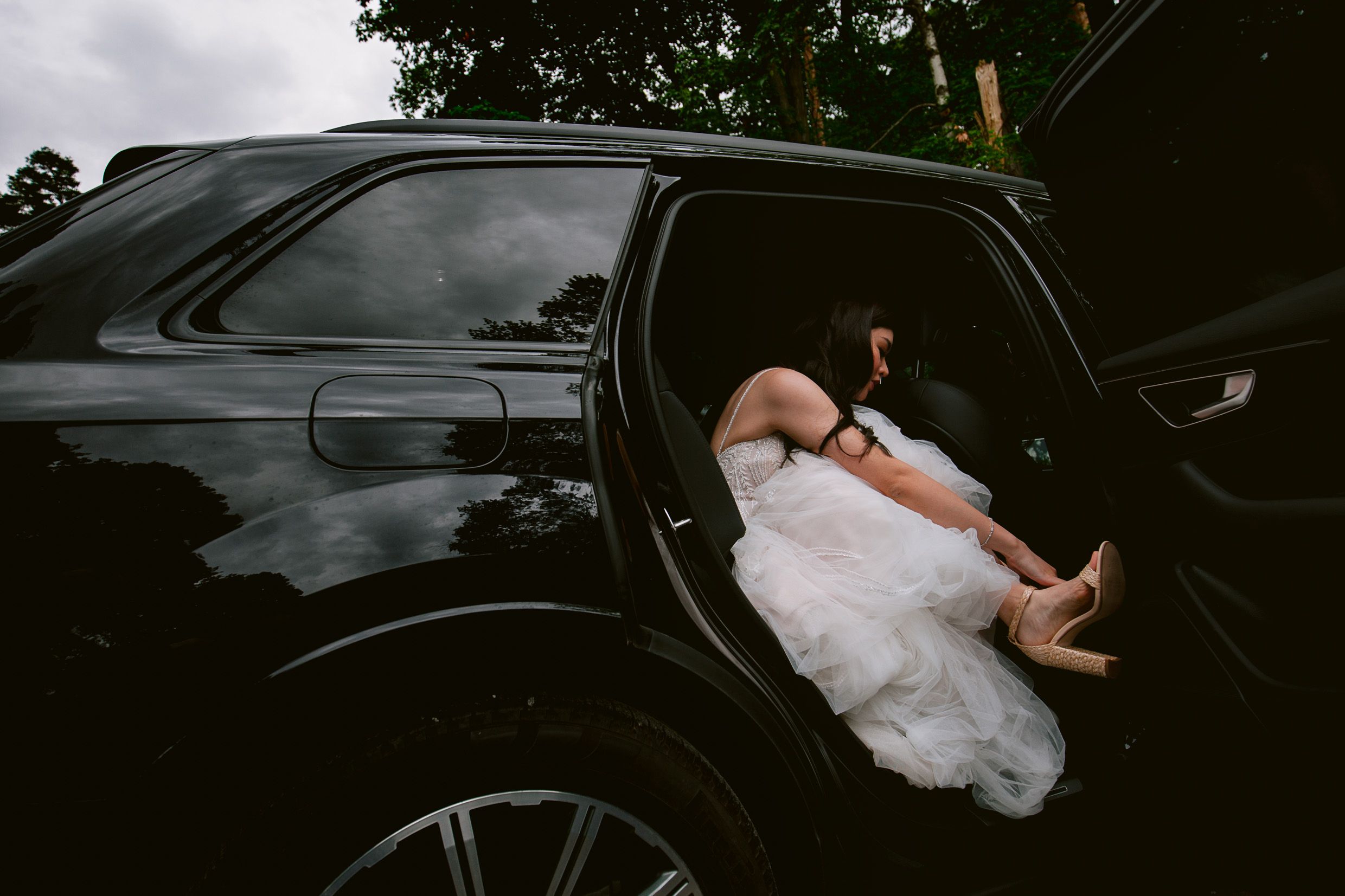 White dress flowing out of black car door in artistic wedding photograph.