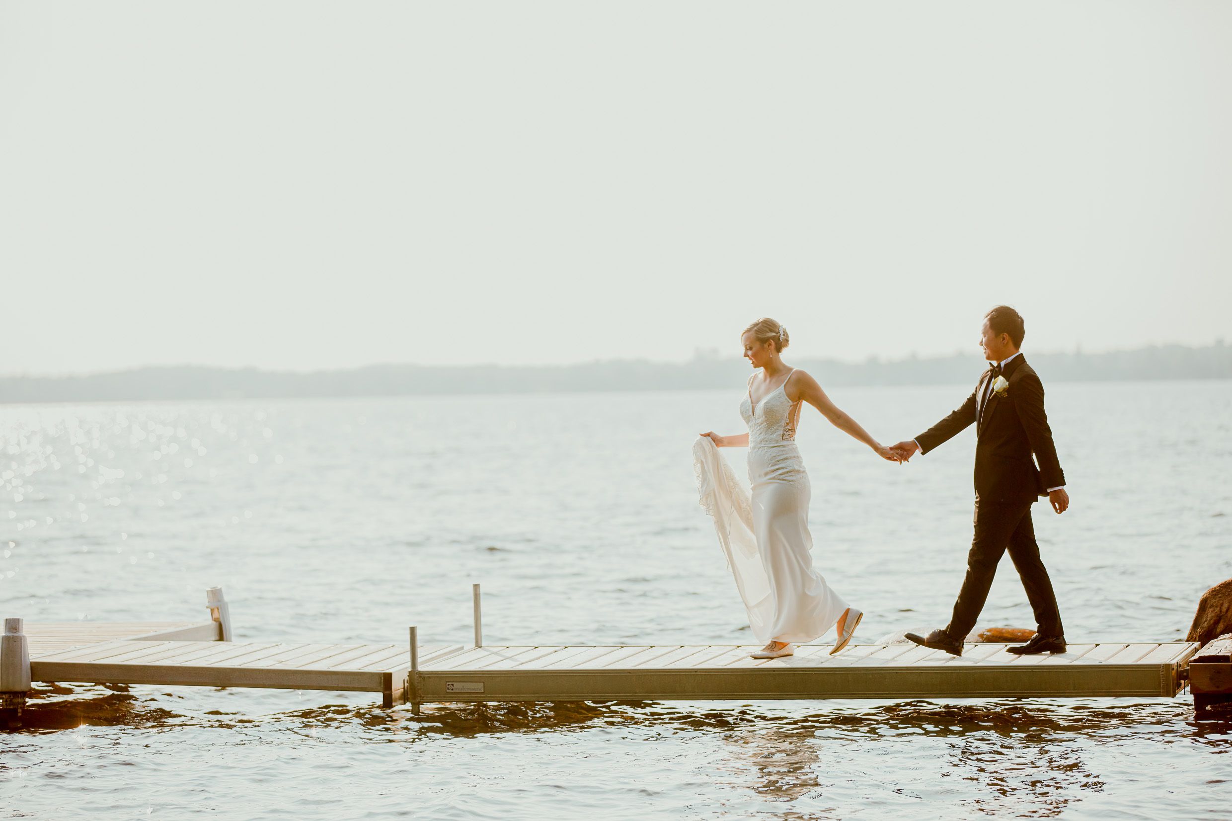 Couple walking hand in hand on a wooden dock by the water.