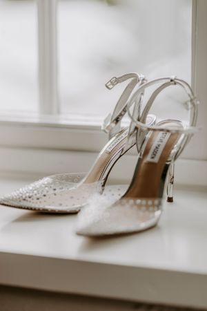 Elegant white beaded bridal heels sit on windowsill in natural light.
