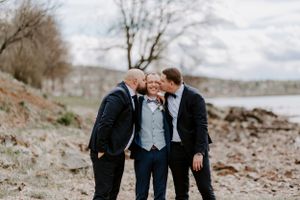 Three people share a lighthearted moment on a rocky beach shoreline.