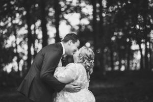Black and white portrait of wedding couple embracing in forest setting.